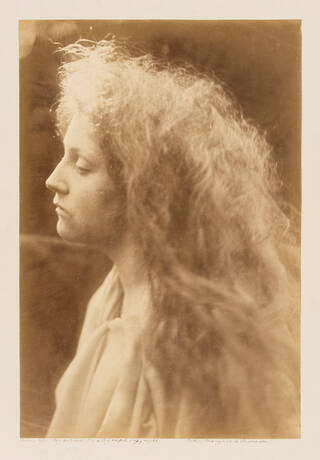Portrait of woman/girl side-on. She has wavy hair and has a neutral expression.